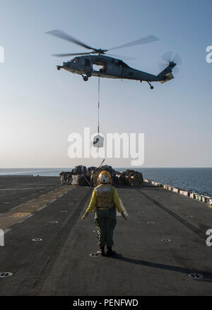 A landing support Sailor with Amphibious Squadron (PHIBRON) 4 directs an SH-60 Seahawk with the squadron while it delivers a package during an aerial resupply aboard the amphibious assault ship USS Kearsarge Jan. 12, 2015, in the Gulf of Oman. Combat Cargo Marines with the 26th Marine Expeditionary Unit (MEU) provided support and transported delivered packages. The 26th MEU and PHIBRON 4 are embarked on the Kearsarge Amphibious Ready Group and are deployed to maintain regional security in the U.S. 5th Fleet area of operations. (U.S. Marine Corps photo by Cpl. Joshua W. Brown/Released) Stock Photo