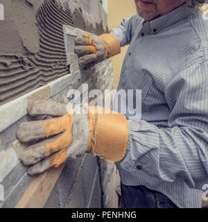 Closeup of manual worker in protection gloves pushing the tile into the cement on the wall while tiling a wall with ornamental tiles, retro effect fad Stock Photo