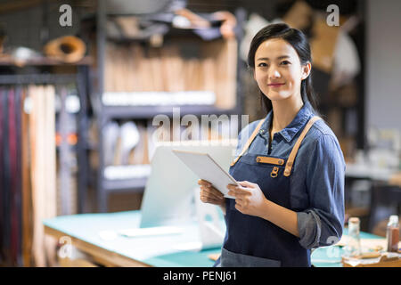 Confident leather craftswoman holding a digital tablet in studio Stock Photo