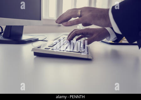 Businessman typing on a computer keyboard on a white desk or office table with foreground copy space in a close up view of his hands, retro toned imag Stock Photo