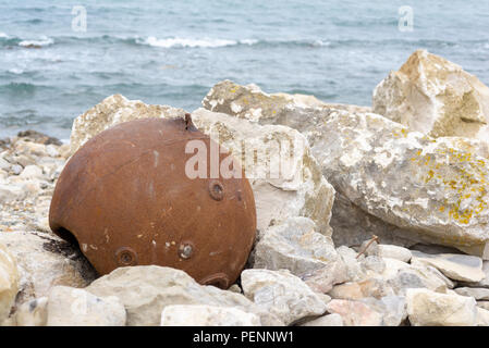 Rusty old sea mine casing on the rocks on the beach Chapman's Pool, Jurassic Coast, Purbeck, Dorset, England, UK Stock Photo