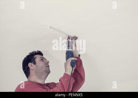 Retro effect faded and toned image of electrician using an electric drill to drill a hole in the ceiling of a building. Stock Photo