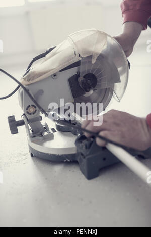 Retro effect faded and toned image of a workman using an electric circular saw to cut a length of plastic profile. Stock Photo