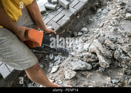 Workers use Electric Concrete Breaker. Male worker repairing driveway surface with jackhammer, digging and drilling concrete roads during sidewalk construction works Stock Photo