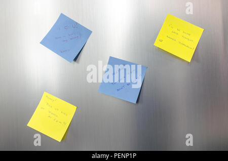 Reminder sticky notes with handwritten text hanging on a stainless fridge. Stock Photo