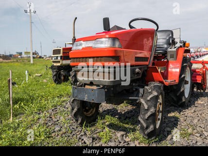 A small mini red tractor stands on a farm yard on green grass and waits for work to begin Stock Photo