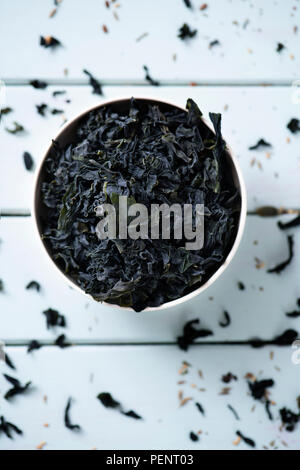 high angle view of a pile of dried leaves of wakame, an Asian edible seaweed used in traditional soups such as the miso soup, on a white ceramic bowl, Stock Photo