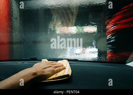 closuep of a young caucasian man dusting the dashboard of a car while this is being washed in a tunnel Stock Photo