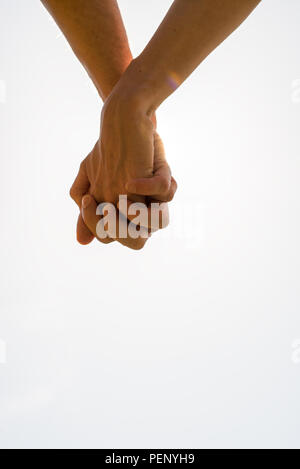 Couple with clasped hands in a closeup conceptual image of love and friendship with plenty of copyspace. Stock Photo