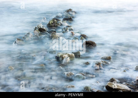 Romantic atmosphere in peaceful morning at sea, water flowing over stones and rocks, long exposure for effect, intentional water blur, fine art Stock Photo