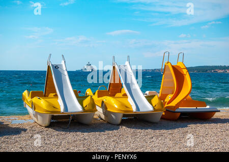 Colorful pedal boats, pedolinos on beach, yellow color, boat with slide, sea in the background Stock Photo