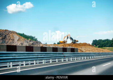 Two heavy, yellow and black excavators on construction site moving soil and rock, highway, road construction, booms are crossed Stock Photo