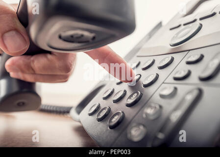 Closeup of male hand holding telephone receiver while dialing a telephone number to make a call using a black landline phone. With retro filter effect Stock Photo