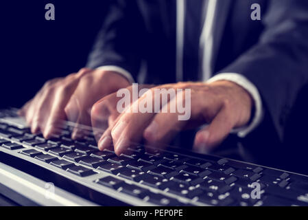 Closeup of the hands of a businessman in a suit typing on a computer keyboard inputting data with motion blur, retro effect faded look. Stock Photo