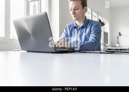 Portrait of a businessman in office typing information on laptop computer keyboard, low angle view from the back of the computer. Stock Photo