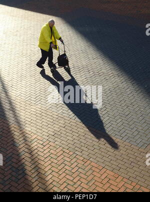 Long shadow of an old man with tri wheel walker on the brick pavement Stock Photo