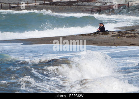 Aberystwyth  Wales UK , Thursday  16 August 2018.  UK Weather: A couple sit on the beach experiencing the waves and strong winds on Cardigan Bay,  Aberystwyth on the west coast of Wales  photo © Keith Morris / Alamy Live News Stock Photo