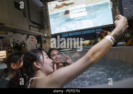 Tokyo, Japan. 17th Aug, 2018. People pose for a selfie during a movie projection on the rooftop of the revamped MAGNET by Shibuya109 building in Tokyo. Bathtub Cinema is held for the first time in Japan, which original concept is from London, people gathering to enjoy a movie and cool off on a outdoor bathing to escape from the high temperatures of this year that has sent thousands of people to the hospital for heatstroke. The event is held until August 19. Credit: Rodrigo Reyes Marin/ZUMA Wire/Alamy Live News Stock Photo
