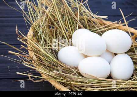 chicken eggs in a basket with hay on a black wooden background. eggs on the hay Stock Photo