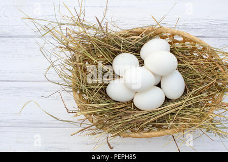 chicken eggs in basket with hay on a white wooden background. eggs on the hay Stock Photo