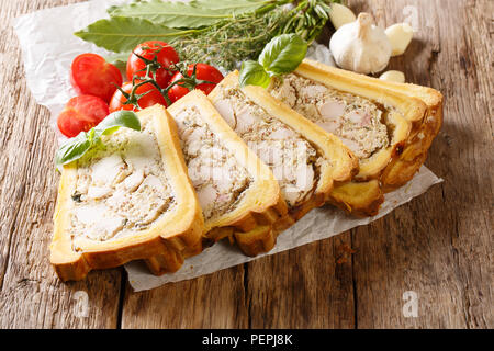 Brioche with a filling of chicken terrine with spices, garlic and herbs close-up on paper on a table. horizontal Stock Photo