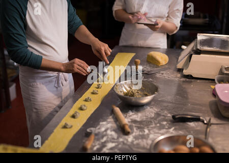 Baker preparing pasta while co-worker using digital tablet his beside Stock Photo