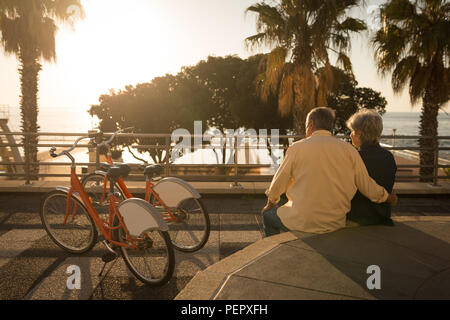 Senior couple sitting on seat wall at promenade Stock Photo