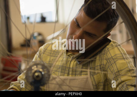 Man talking on mobile phone while repairing bicycle in workshop Stock Photo