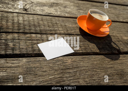 Blank paper next to orange cup of coffee on old wooden desk. Stock Photo