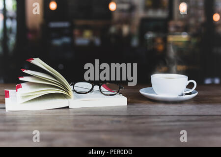 Selected focus of coffee cup with open book and glasses on wooden table in matte color. Stock Photo