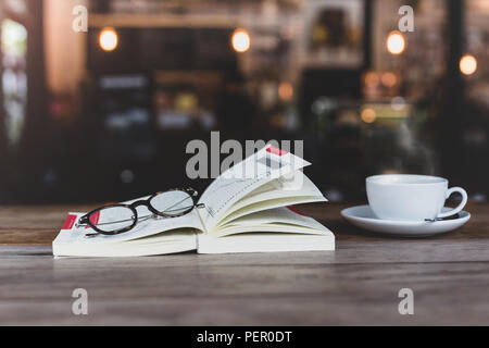 Selected focus of glasses on open book with cup of coffee on wooden table. Stock Photo