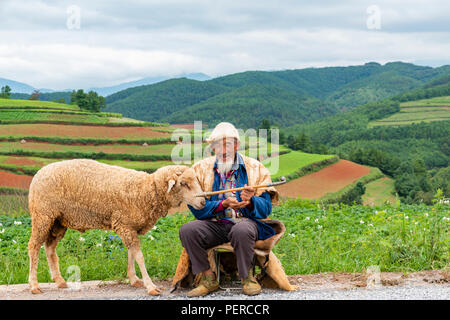 An old Chinese man dressed with the traditional clothing  smoking while enjoying the scenery of DongChuan in Yunnan Province, China Stock Photo