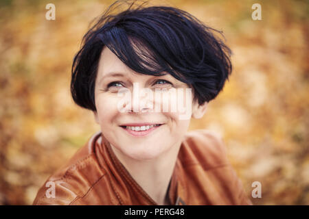 Closeup portrait of middle aged caucasian dark haired brunette woman with short bob hairstyle in light brown leather jacket  looking up smiling outsid