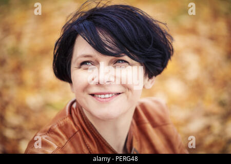 Closeup portrait of middle aged caucasian dark haired brunette woman with short bob hairstyle in light brown leather jacket  looking up smiling outsid Stock Photo