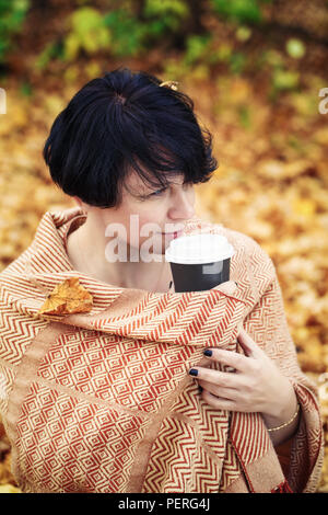 Portrait of middle aged caucasian dark haired brunette woman with short bob hairstyle, yellow orange woolen scarf on her body sitting on ground outsid Stock Photo