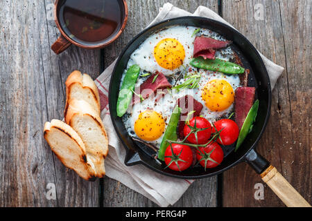 Fried eggs in a frying pan with cherry tomatoes, green peas and pastrami. Copyspace Stock Photo