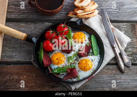 Fried eggs in a frying pan with cherry tomatoes, green peas and pastrami. Copyspace Stock Photo