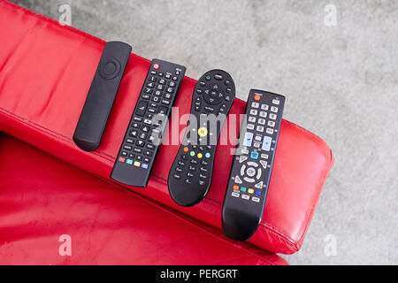 TV digital wireless remote controls on red sofa chair arm Stock Photo