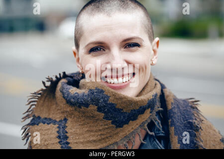 Closeup portrait of happy smiling laughing beautiful Caucasian white young bald girl woman with shaved hair head in leather jacket and scarf shawl loo Stock Photo