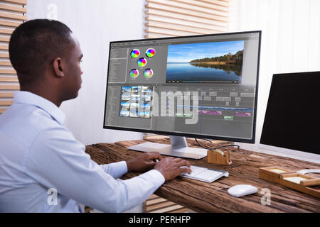 An African American Businessman Editing The Video On Computer Over The Wooden Desk Stock Photo