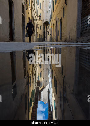Florence, Italy - March 30, 2018: A pedestrian walks past traditional closely-built Renaissance-era houses reflected in a puddle on a street in Floren Stock Photo