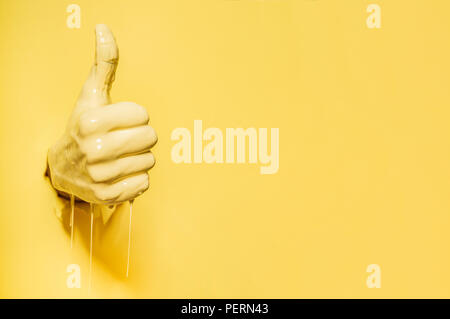 Hand showing the 'like' sign comes out of the yellow wall Stock Photo