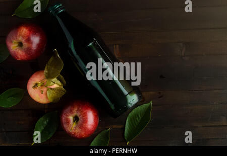 A bottle of a apple cider vinegar with three fresh apples and green leaves on wooden background.Copyspace right. Stock Photo