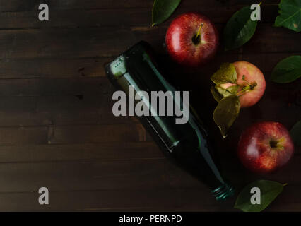 A bottle of a apple cider vinegar with three fresh apples and green leaves on wooden background..Copyspace left. Stock Photo