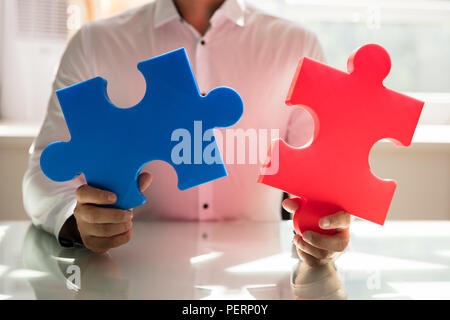 Businessman's hand connecting two colorful jigsaw puzzles in office Stock Photo