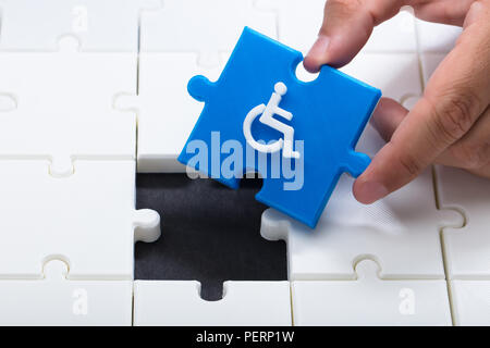 Human hand solving jigsaw puzzle with blue piece having handicap icon Stock Photo