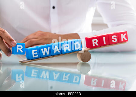 Businessman's hand showing unbalance between reward and risk on wooden seesaw Stock Photo