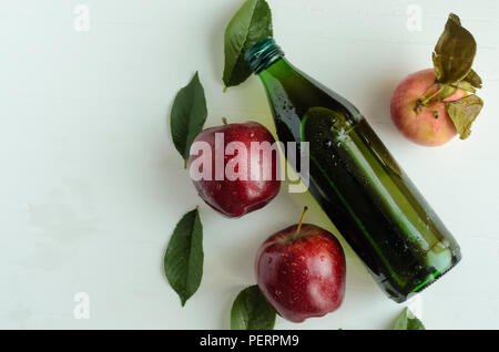 A bottle of a apple cider vinegar with three fresh apples and green leaves on white background.Copyspace left. Stock Photo