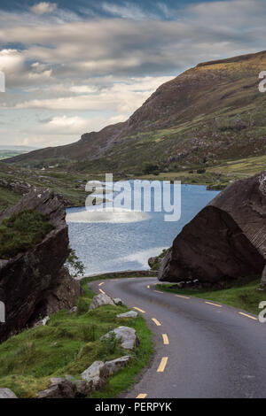 A narrow lane winds through the mountain pass and past Augher Lake in the Gap of Dunloe, nestled in the Macgillycuddy's Reeks mountains in Ireland's C Stock Photo