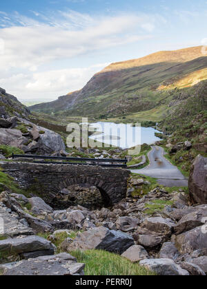 A narrow lane winds through the mountain pass and past Augher Lake in the Gap of Dunloe, nestled in the Macgillycuddy's Reeks mountains in Ireland's C Stock Photo